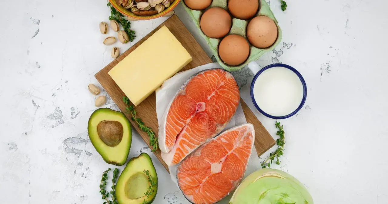 Składniki na dietę keto: łosoś, awokado, jajka, ser, masło, mleko, pistacje i kalarepa.